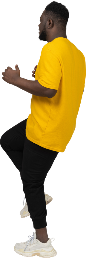 Vista lateral de un joven de piel oscura con camiseta amarilla levantando la pierna