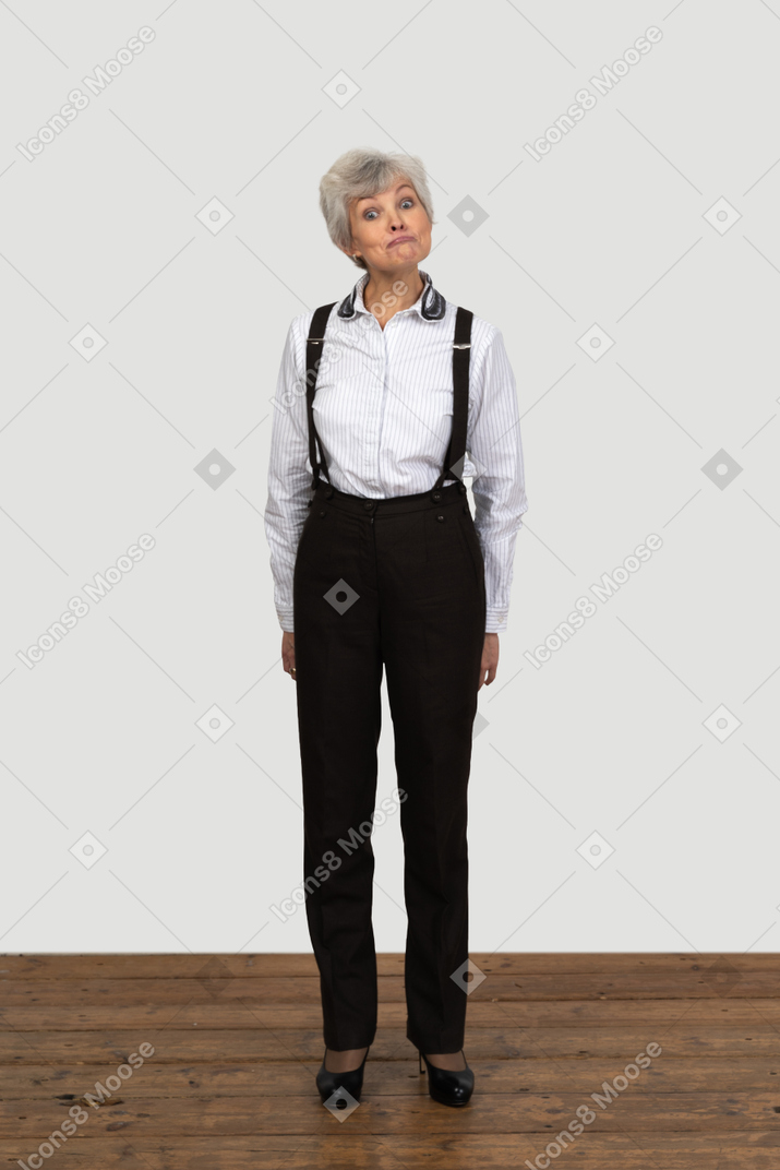 一位老惊讶的女性，在办公室的衣服做鬼脸，用她的双手背后的前视图
