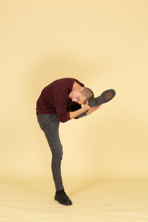 Three-quarter view of a young man in red pullover stretching his leg