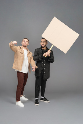 Vista frontale di due giovani che sventolano un cartellone pubblicitario in modo aggressivo