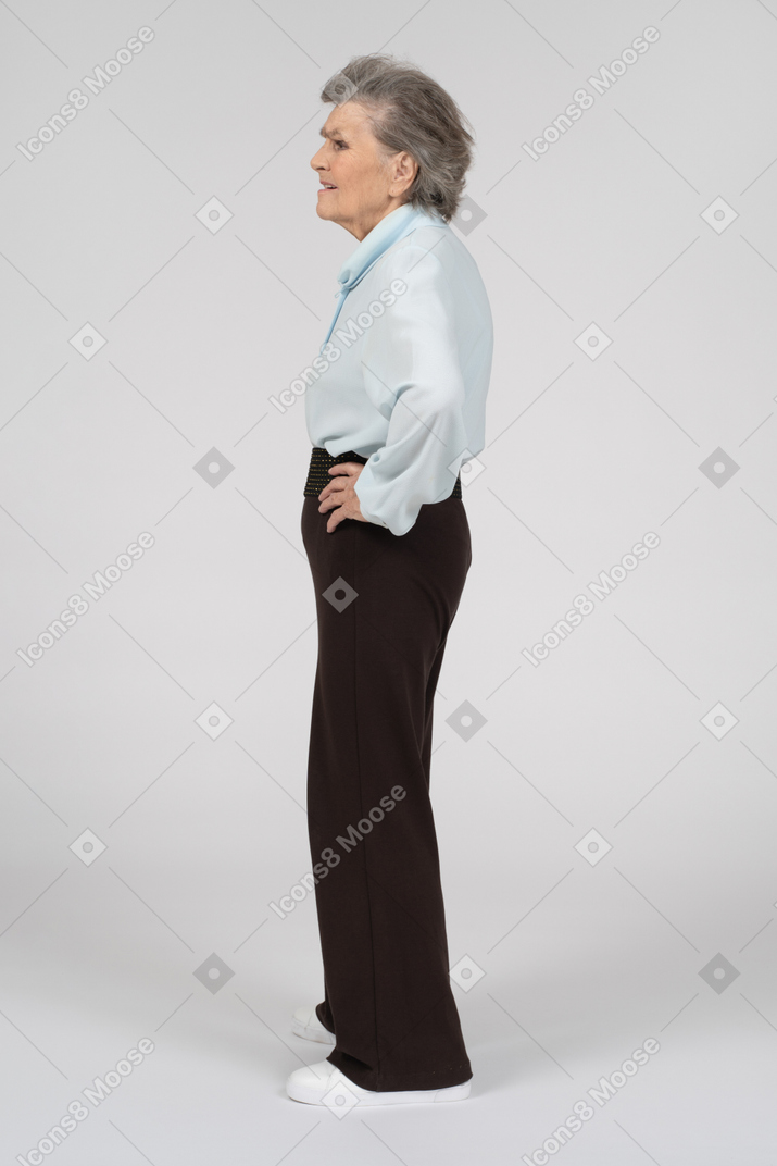 Vista lateral de una anciana que parece desconcertada con una mano en la cadera