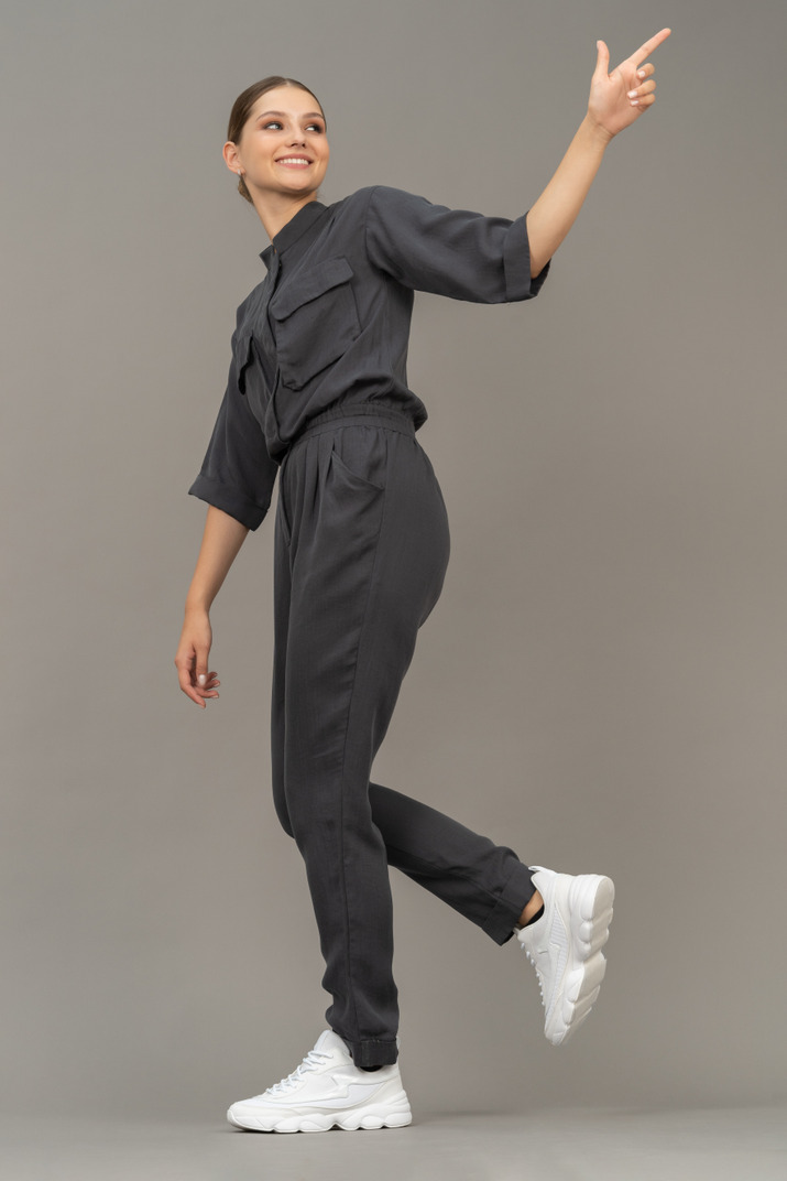 Side view of a cheerful young woman in a jumpsuit outstretching her arm