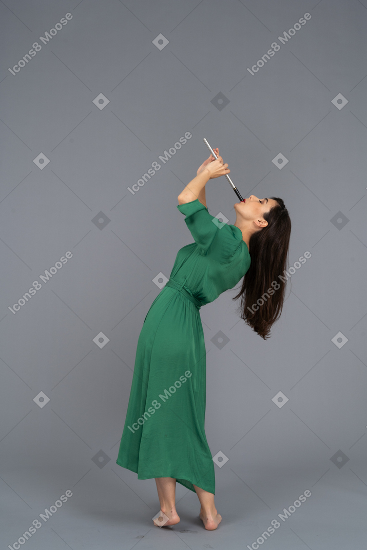 Vista laterale di una giovane donna in abito verde che suona il flauto mentre si appoggia indietro