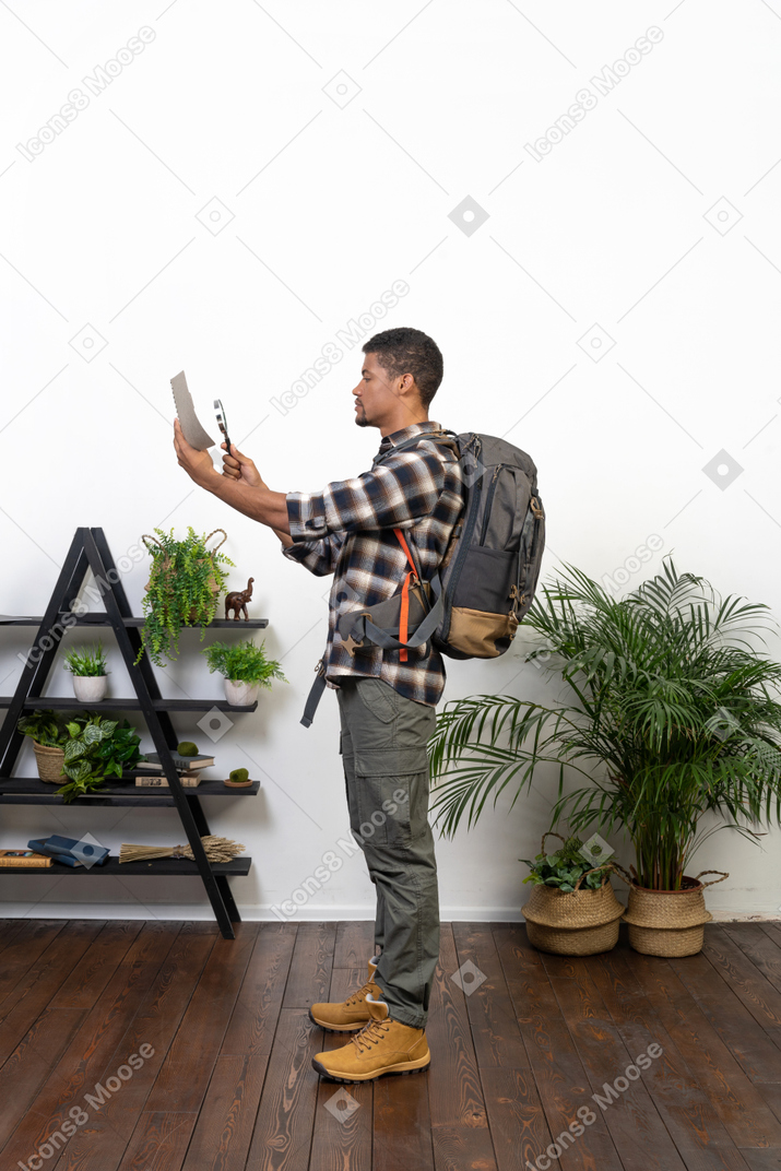 Vista lateral de un turista con una mochila examinando el mapa a través de una lupa