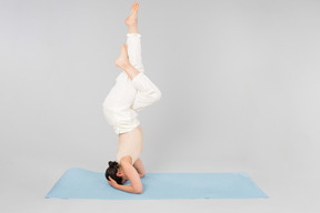 Jeune femme debout sur la tête sur un tapis de yoga