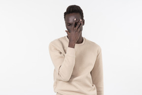 Un joven negro en un suéter gris de pie solo sobre el fondo blanco.