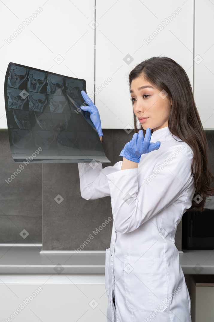 Vista lateral de una doctora desconcertada sosteniendo una imagen de rayos x y mirando a un lado