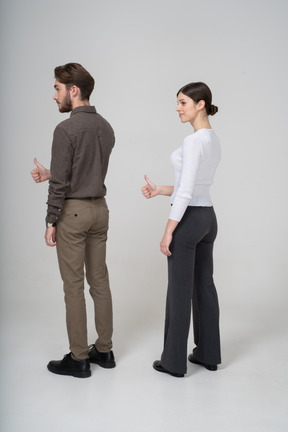 Three-quarter back view of a cheerful young couple in office clothing showing thumb up
