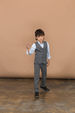 Вид спереди милого мальчика в сером костюме, указывающего пальцем
