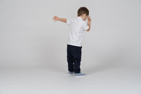 Rear view of a boy standing with his left arm extended