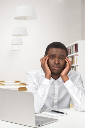 A tired man sitting at a desk with a laptop in front of him