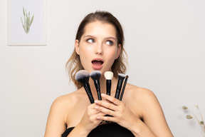 Front view of a surprised young woman holding make-up brushes