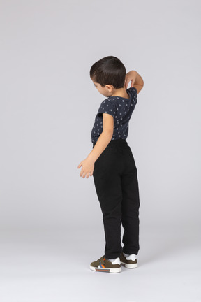 Vista lateral de um menino bonito em roupas casuais coçando as costas