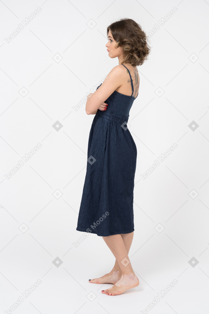 Displeased young woman standing in profile with folded hands