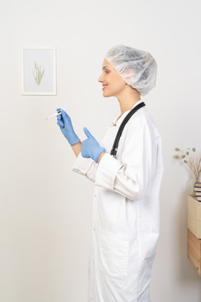 Side view of a young female doctor with stethoscope holding thermometer and showing thumb up