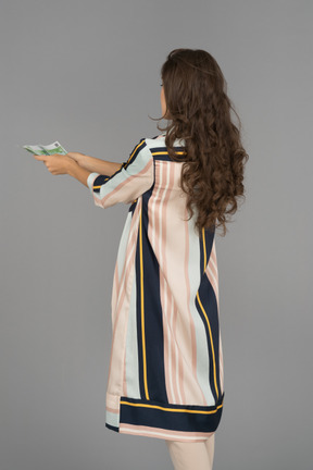 Donna bruna dai capelli lunghi che tende le mani con i soldi indietro alla macchina fotografica