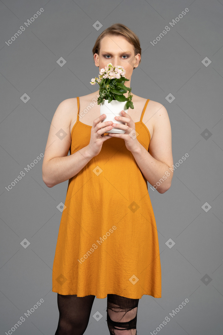 Vista frontal de una persona queer joven en vestido naranja que huele flores