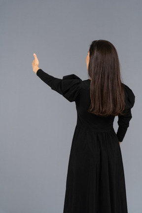 親指を上に表示している黒いドレスを着た若い女性の背面図