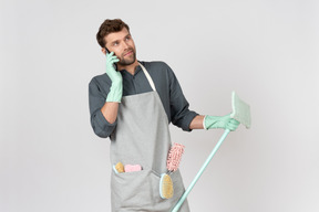 Young househusband holding mop and talking on the phone