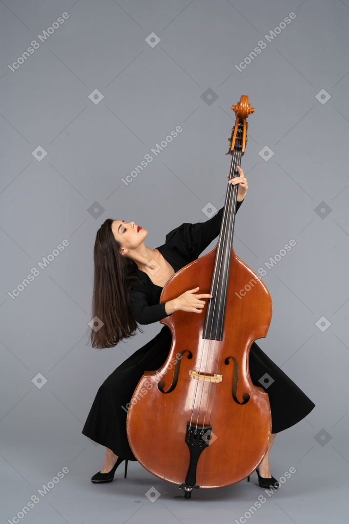 Front view of a graceful squatting young lady standing behind her double-bass