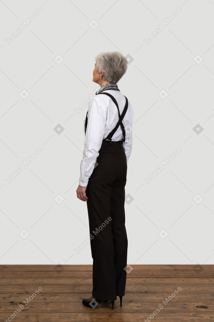 Three-quarters view of an old female with suspenders standing still in an empty room