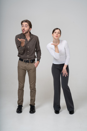 Vista frontal de una joven pareja en ropa de oficina enviando un beso al aire