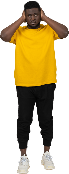 Vista frontal de un hombre de piel oscura con camiseta amarilla bloqueando sus oídos