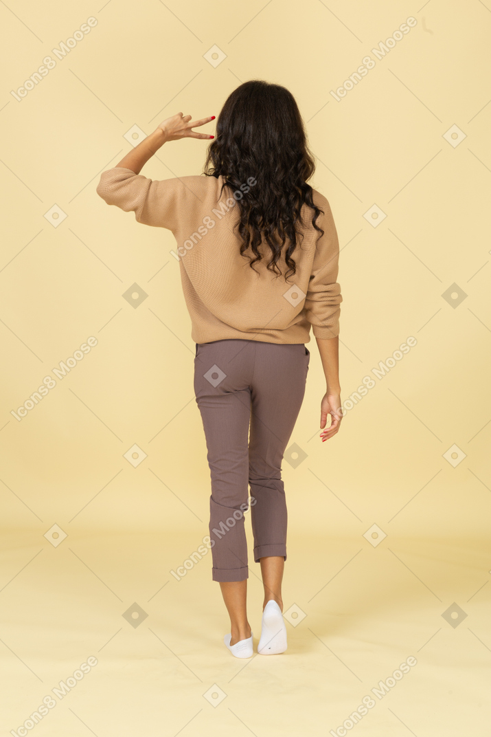 Back view of a dark-skinned young female showing  peace sign