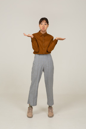 Вид спереди смешной молодой азиатской женщины в бриджах и блузке, поднимающей руки