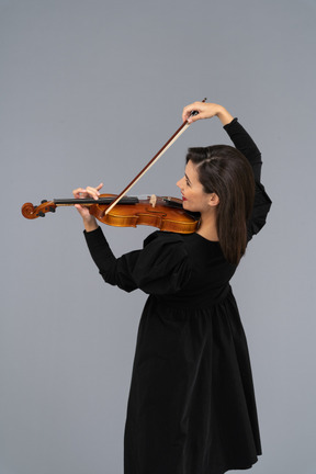 Close-up de uma jovem alegre de vestido preto tocando violino