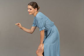 Vista lateral de uma jovem de vestido azul segurando uma escova de dentes e inclinada para a frente