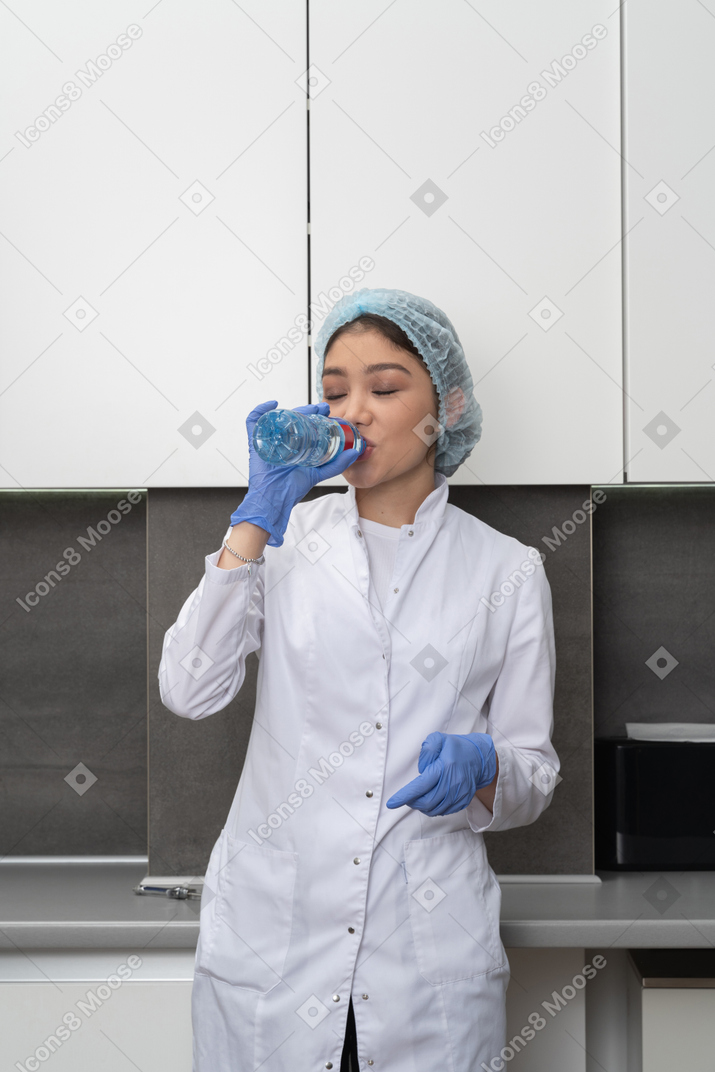 Front view of a female nurse drinking water with her eyes closed