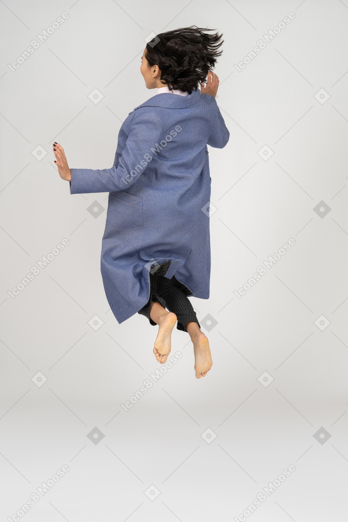 Vista traseira da mulher de casaco pulando