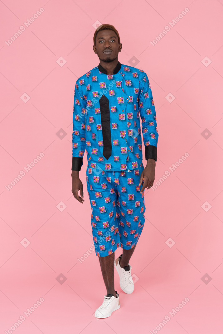 Hombre negro en pijama azul caminando sobre fondo rosa