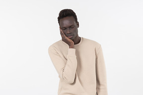 Un joven negro en un suéter gris de pie solo sobre el fondo blanco.