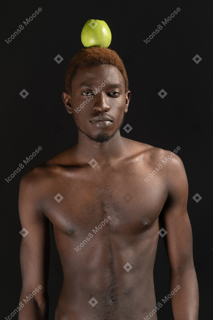 Close-up de um homem africano de pé confiante com uma maçã na cabeça