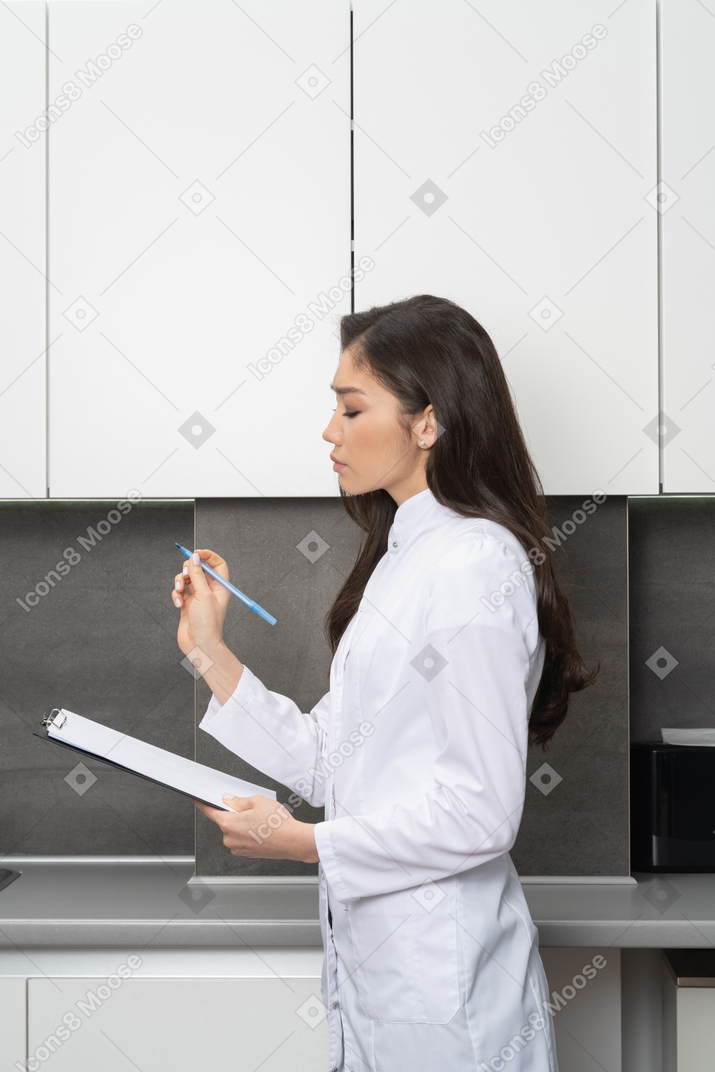 Vista lateral de una doctora tomando notas en su tableta