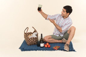 Jeune homme caucasien assis sur une couverture et boire du vin