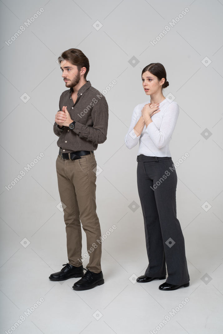Three-quarter view of a worried young couple in office clothing holding hands together