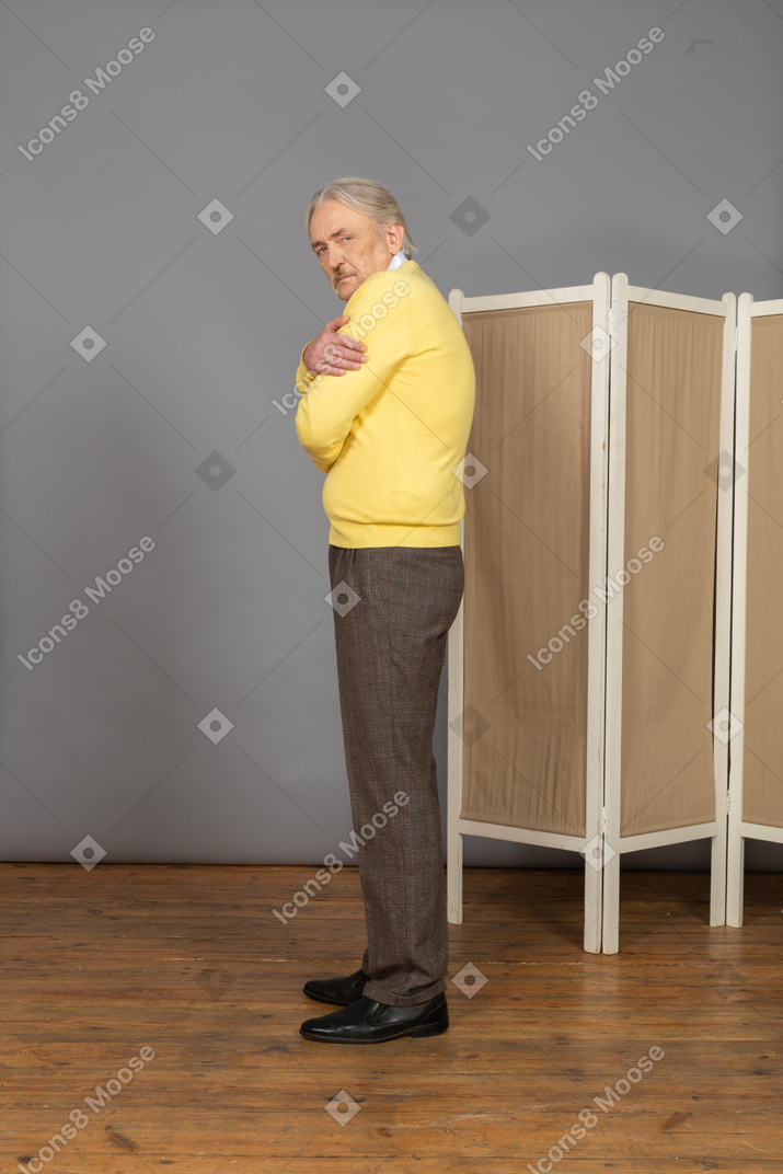 Side view of an old suspicious man embracing himself