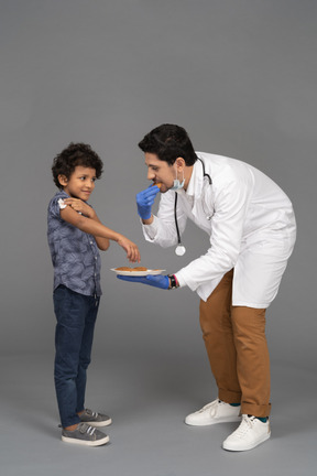 Menino e médico comendo biscoitos após a vacinação
