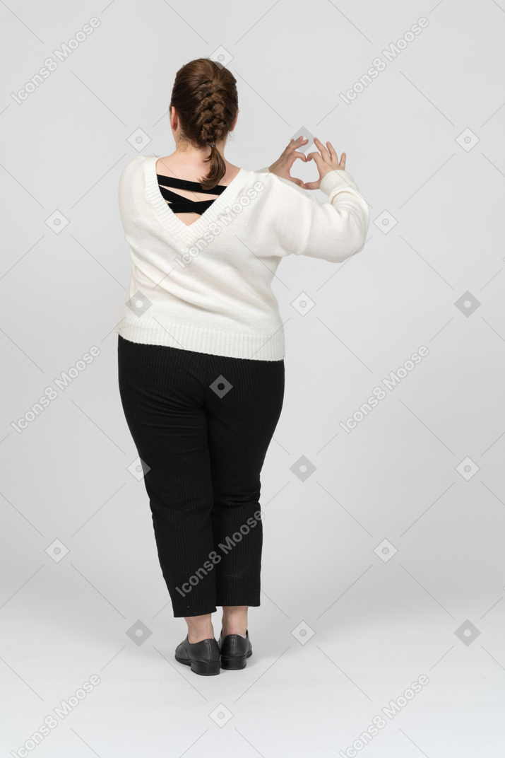 Женщина больших размеров в повседневной одежде показывает фигуру сердца пальцами