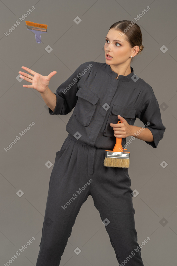 Woman in gray coveralls tossing a paint brush into the air