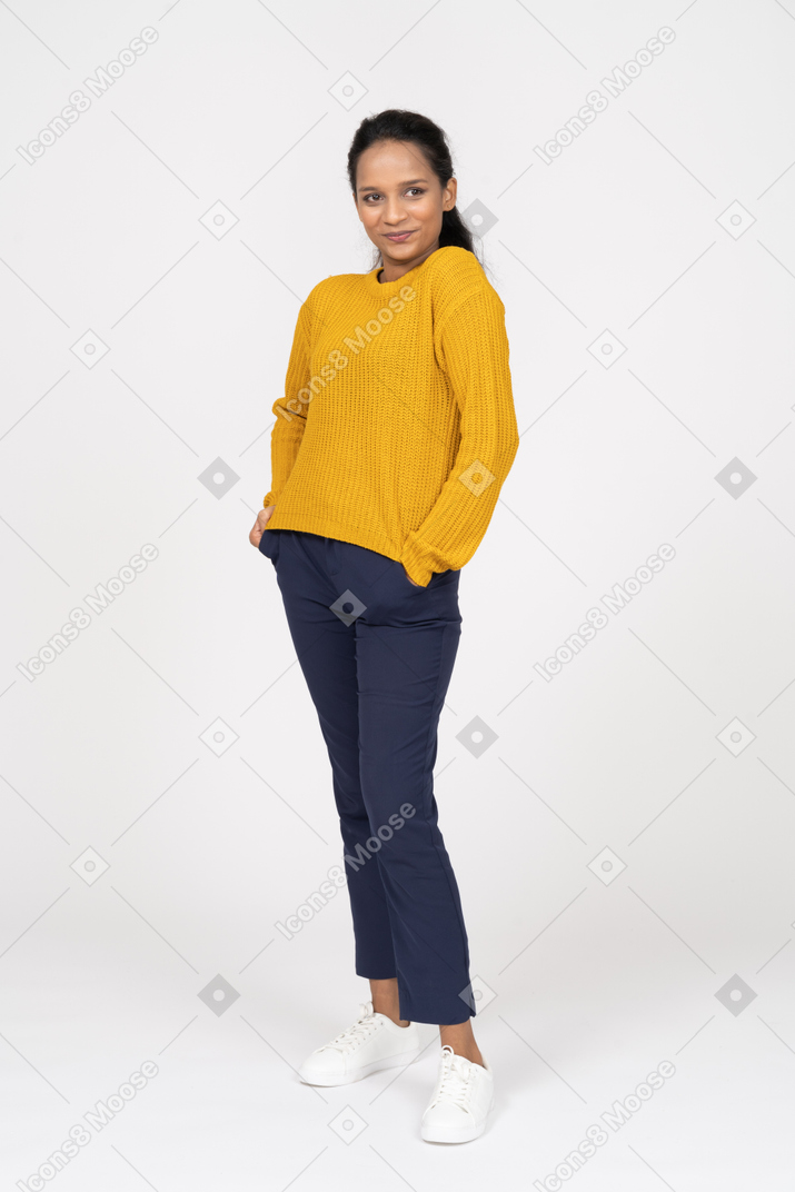 Front view of a girl in casual clothes posing with hands in pockets and looking at camera