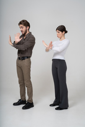 Vista de tres cuartos de una pareja joven en ropa de oficina cruzando los brazos