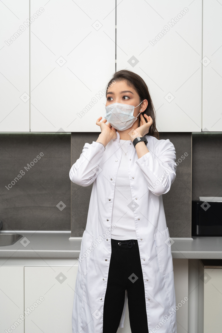 Front view of a female doctor adjusting her protective mask and looking aside