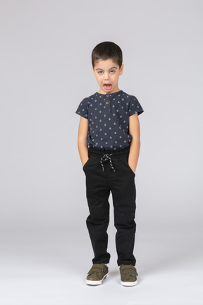 Вид спереди симпатичного мальчика, стоящего с руками в карманах и смотрящего в камеру