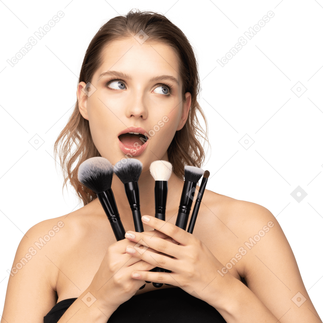 Front view of a surprised young woman holding make-up brushes