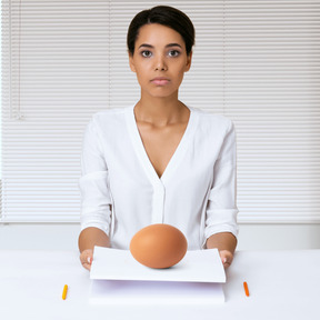 A woman sitting at a desk with an egg in front of her