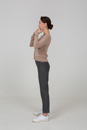 Side view of a young lady in pullover and pants touching her mouth